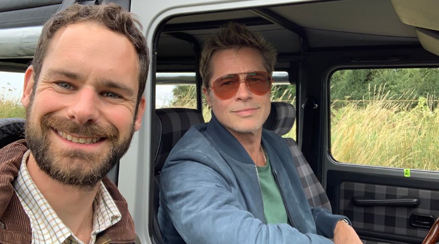 Richard heady smiling next to Brad Pitt sitting in a 4x4